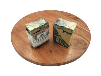 Two bars of soap on a wooden round surface with a white background