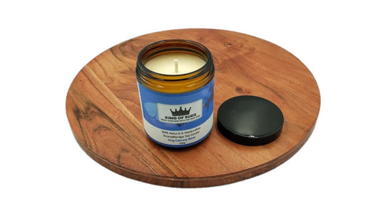 Candle in an amber glass jar on a wooden coaster with a white background