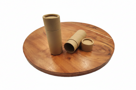 Three small kraft paper cylindrical tubes, including one standing tube, one lying tube, and one small cap, arranged on a round wooden board against a white background.